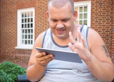 Autistic man typing on a tablet sitting outdoors