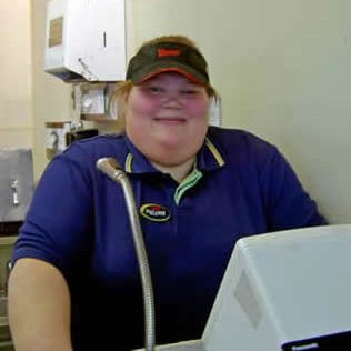 A woman working at a restaurant cash register and smiling.