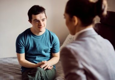 Smiling down syndrome man and his therapist talking during home visit.